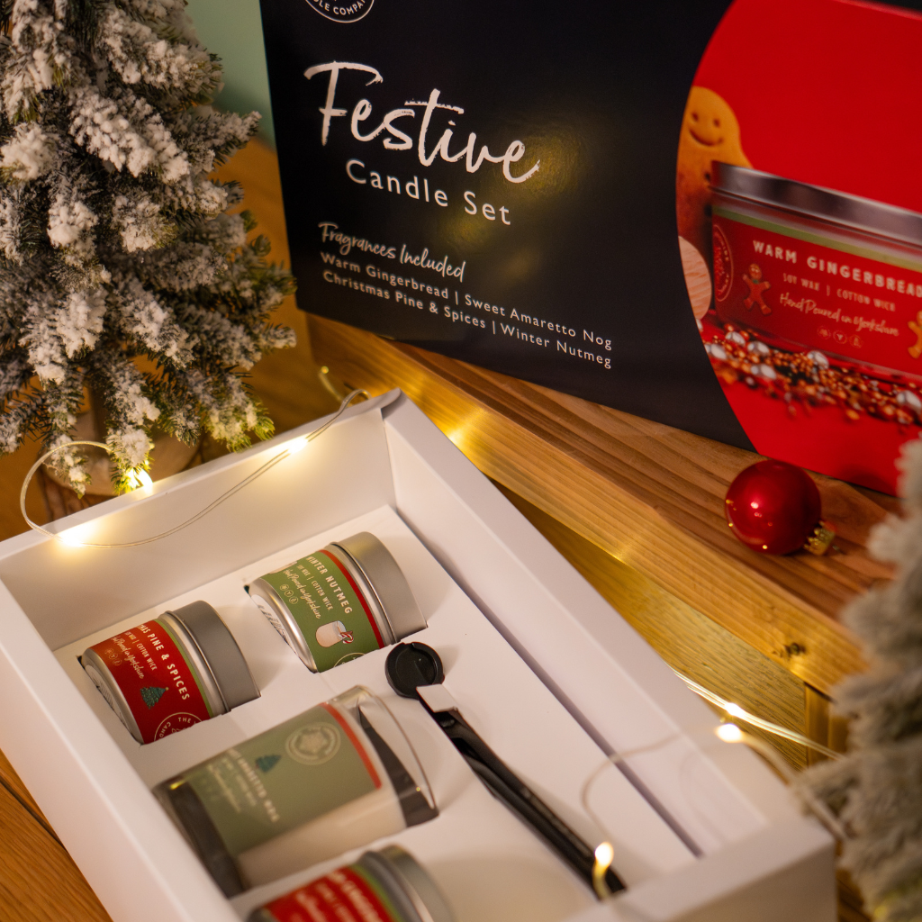 Open festive candle gift set showing candles and a black wick trimmer beside Christmas decorations