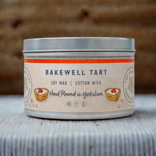 Candle in a tin labeled 'Bakewell Tart' with a rustic background