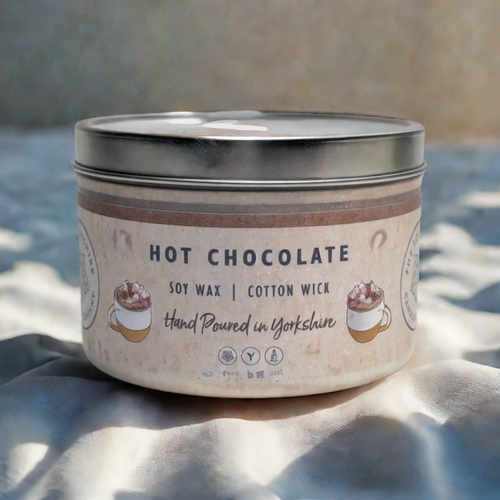 Candle in a tin labeled 'Hot Chocolate' on a textured surface