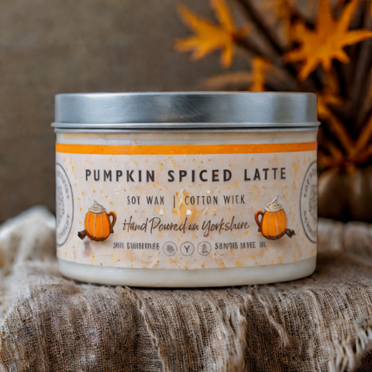 Candle labeled 'Pumpkin Spiced Latte' on a textured surface with autumn leaves in the background