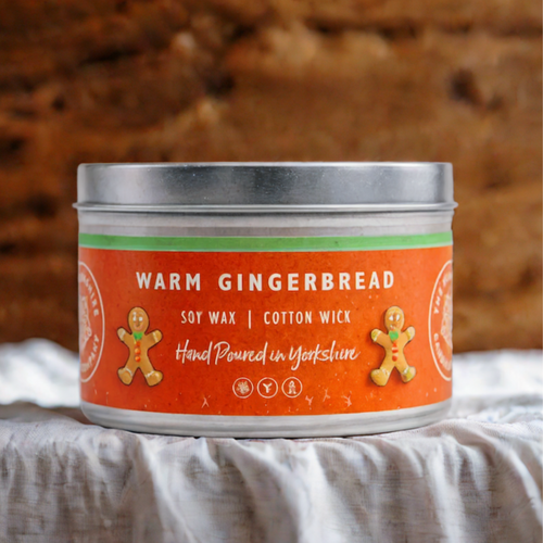 Candle tin labeled 'Warm Gingerbread' with gingerbread men graphics on an orange background.